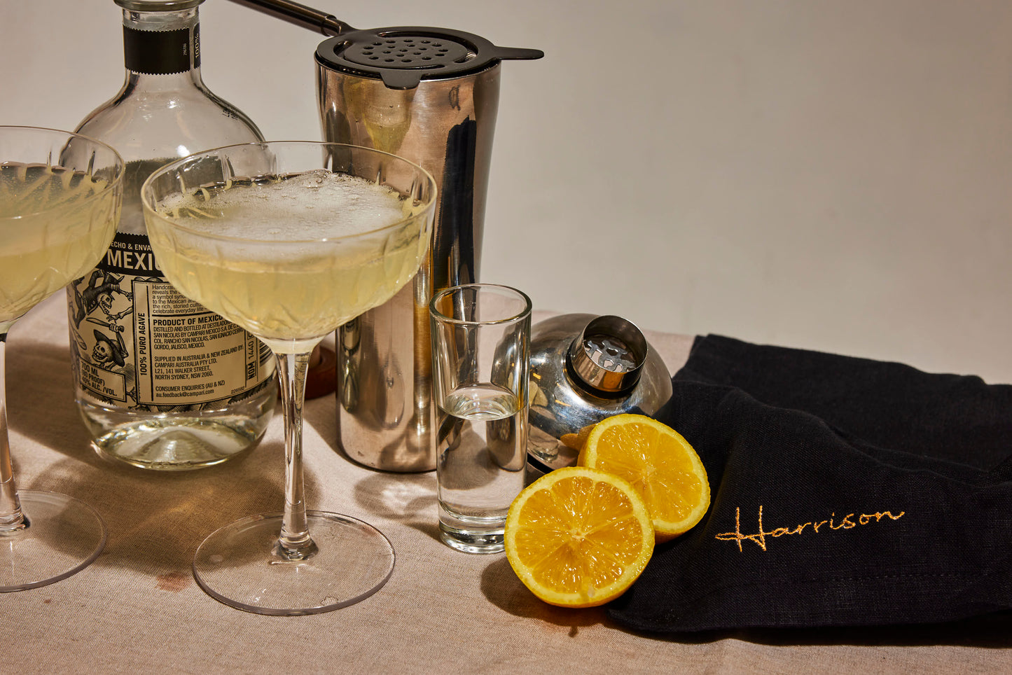 Black linen napkin embroidered Harrison in gold, styled with citrus, tequila, cocktail glasses and a shaker