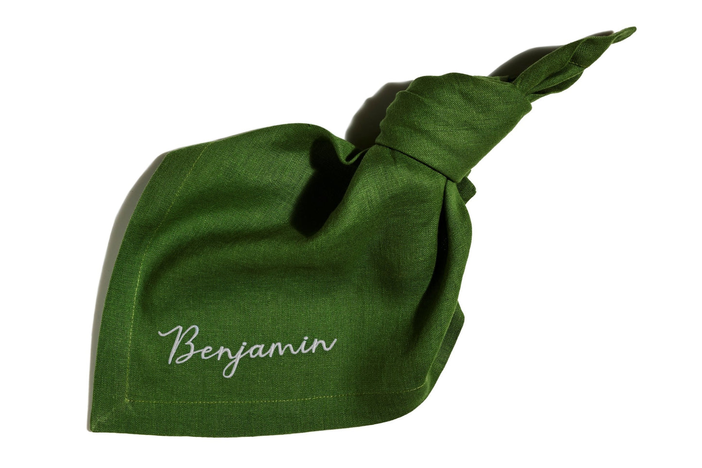 Green linen napkin with knotted corner, featuring custom name embroidery in white thread