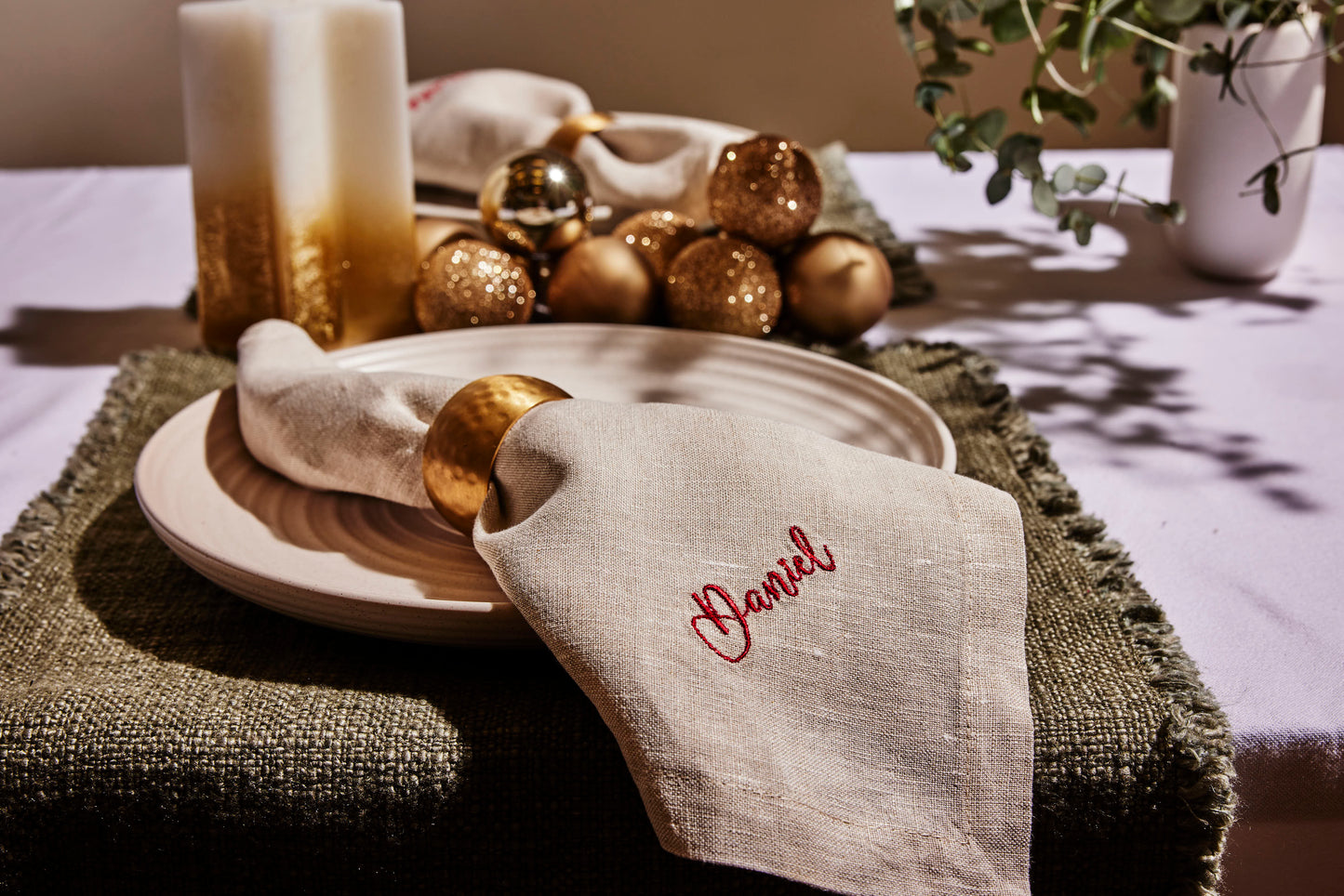 Linen napkin embroidered Daniel in red script, styled with gold napkin ring and Christmas table decor
