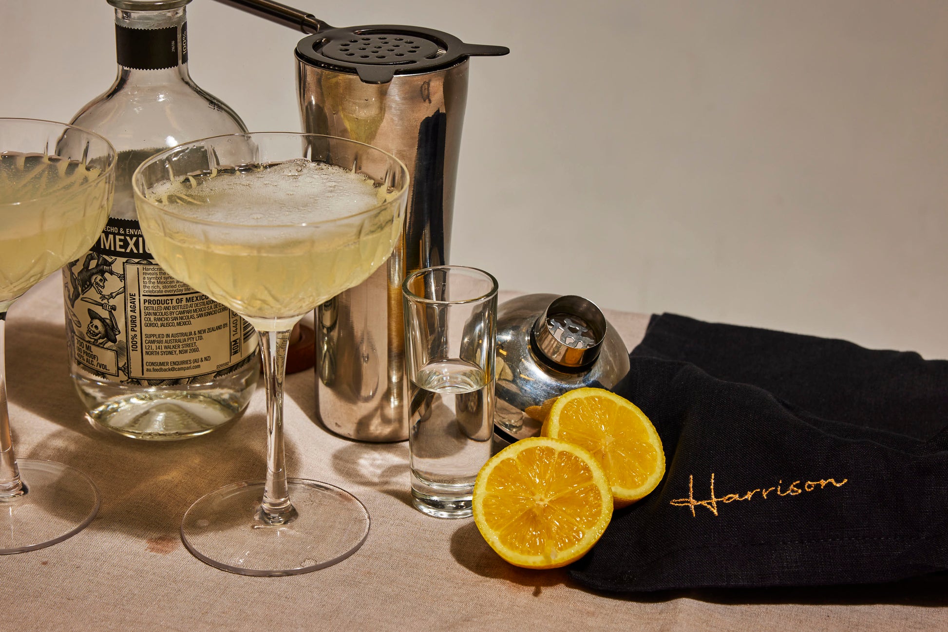 Black linen napkin embroidered Harrison in gold, styled with citrus, tequila, cocktail glasses and a shaker