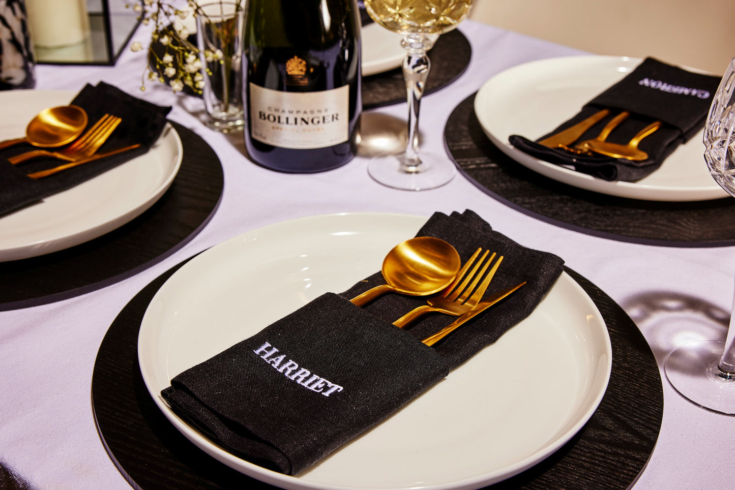 Modern place setting with black embroidered napkin labelled Harriet, gold cutlery and champagne