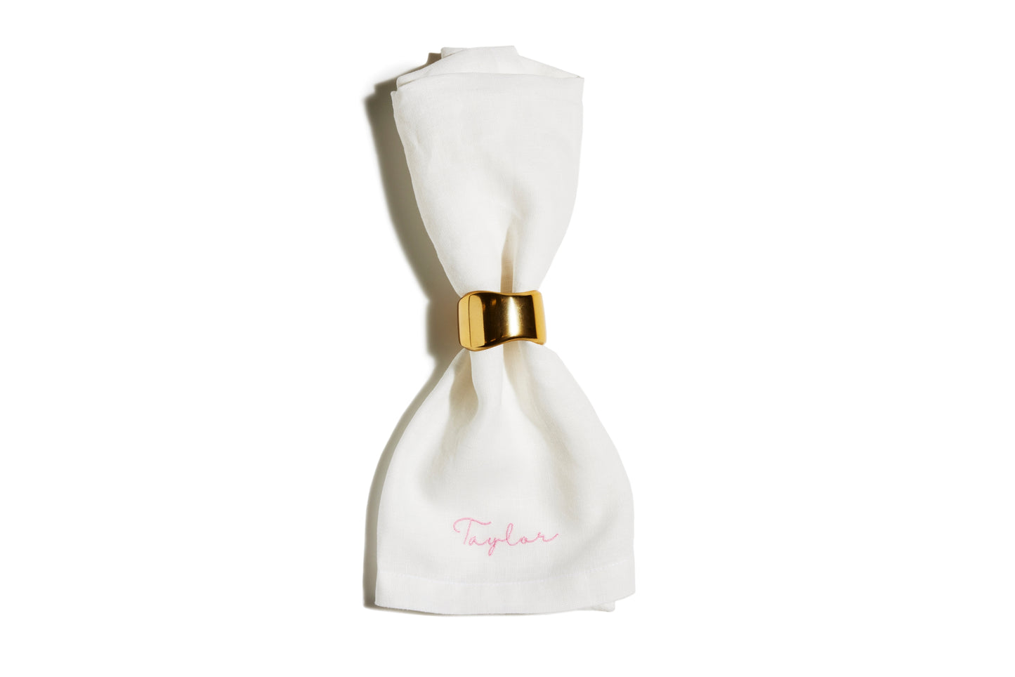 White linen napkin with pink embroidered name Taylor, held by a gold napkin ring
