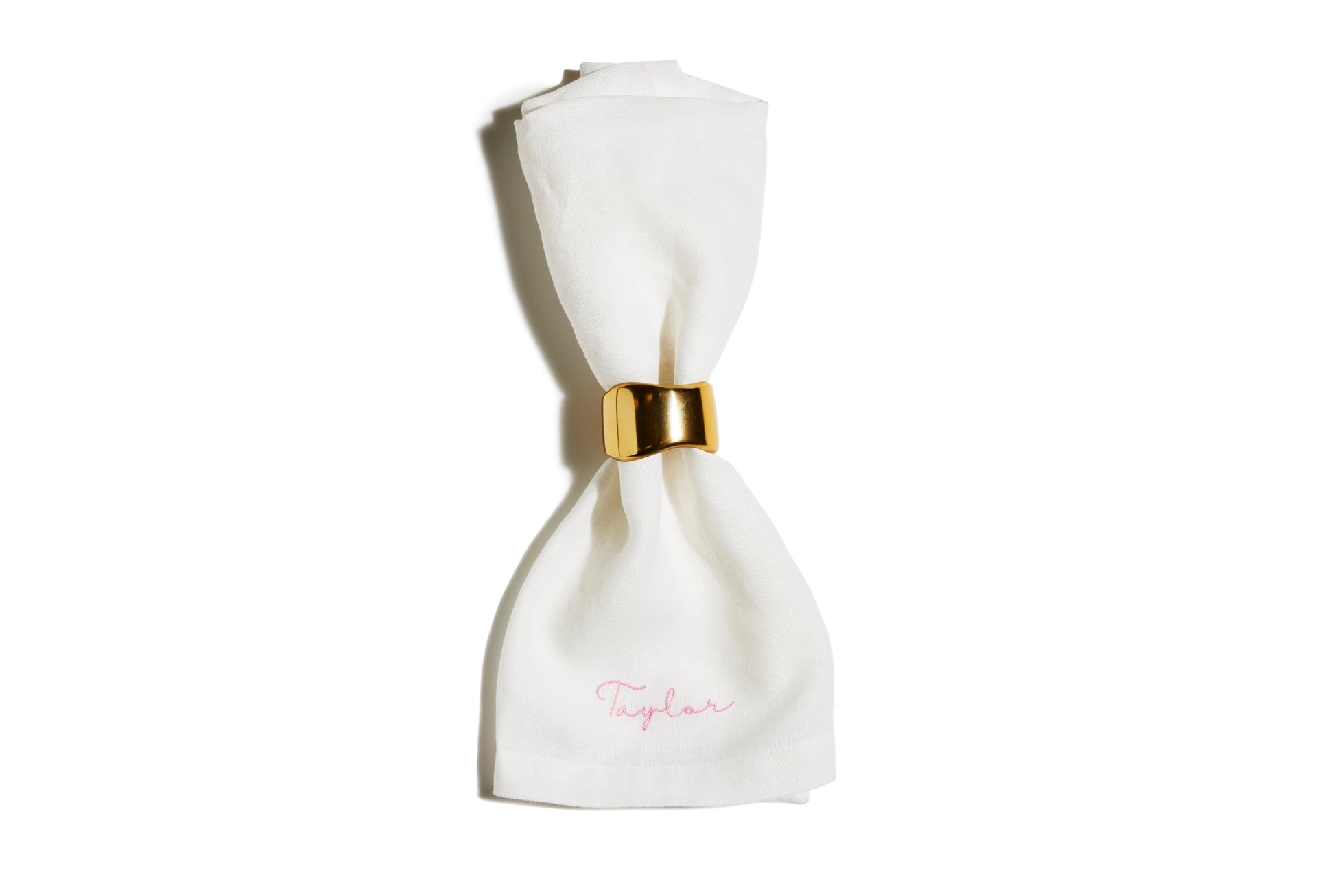 White linen napkin with pink embroidered name Taylor, held by a gold napkin ring
