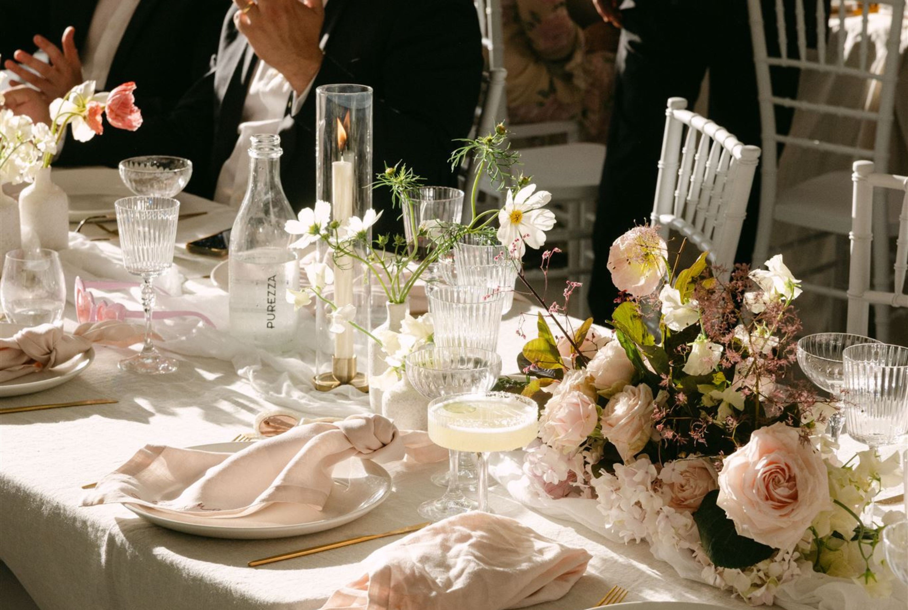 Elegant wedding table setting with blush linen napkins, white flowers, crystal glassware, and a floral centrepiece