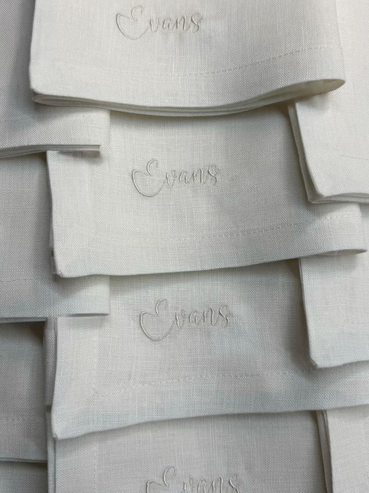 Stacked ivory linen napkins with tonal script embroidery reading Evans on each, neatly folded