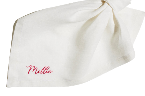 White linen napkin tied in an elegant knot, embroidered with the name Millie in red script.