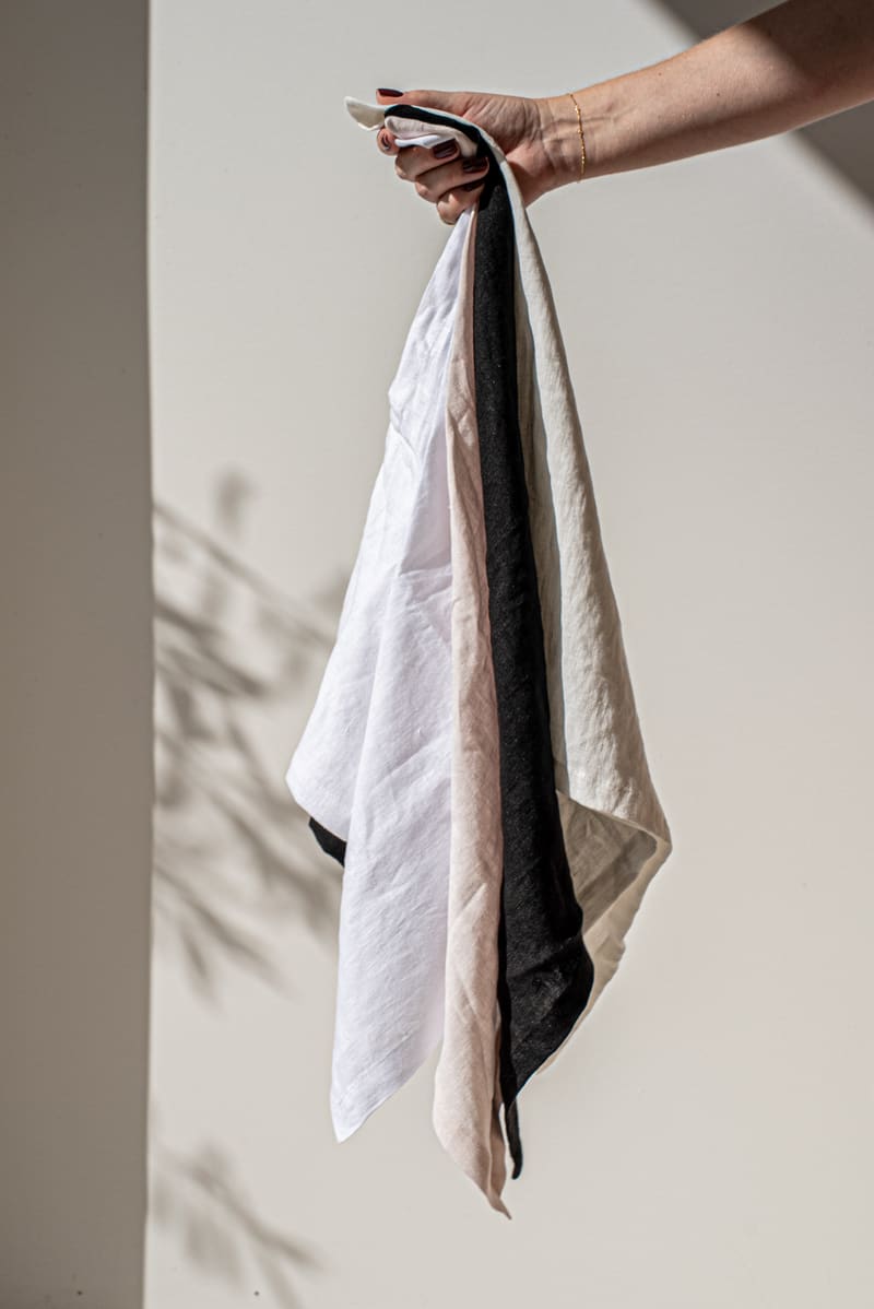 Five pure linen napkins draped together showing the colourways: white, blush, ivory, sand and black.
